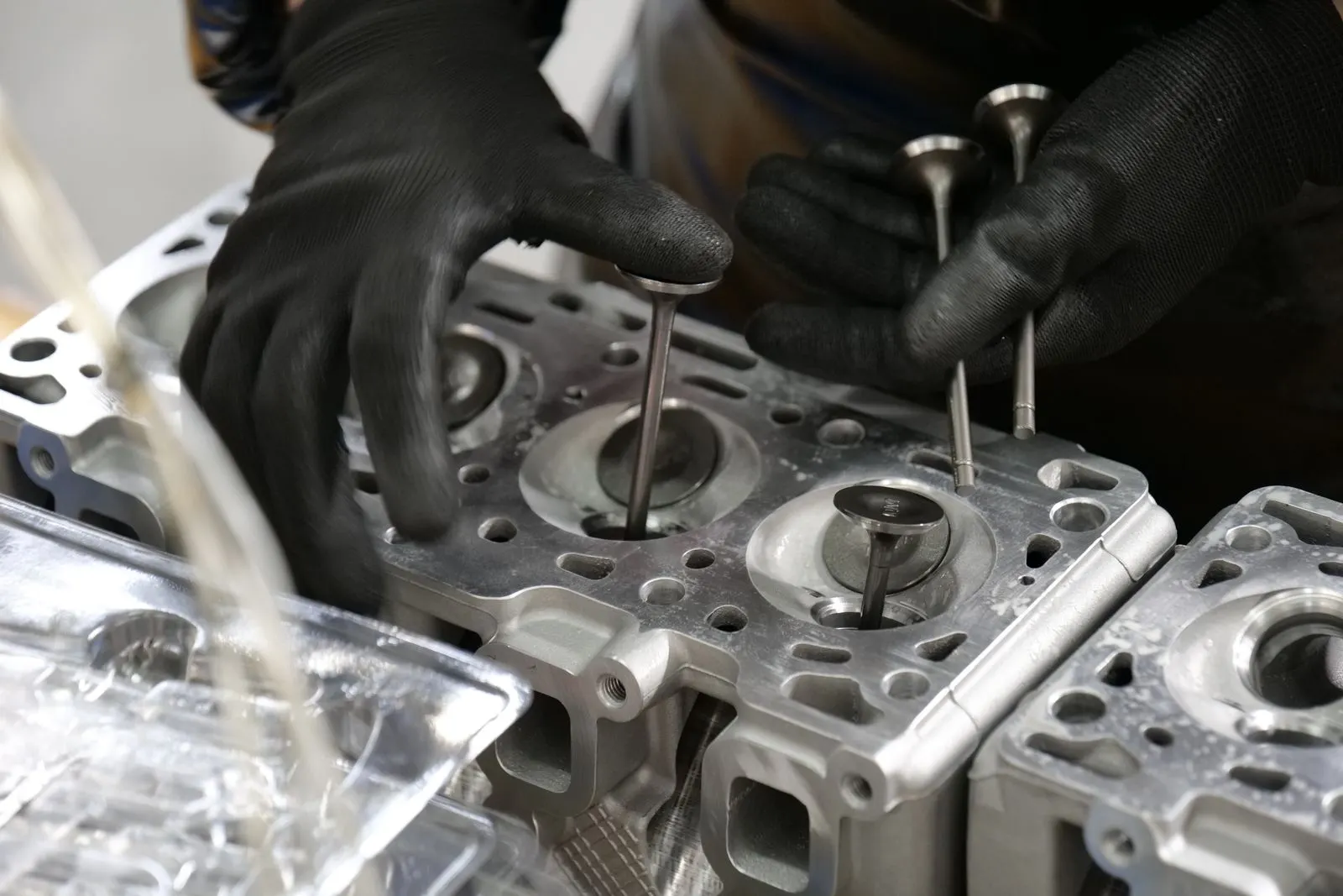 Gloved hands placing valves into an aluminum cylinder head on a workbench