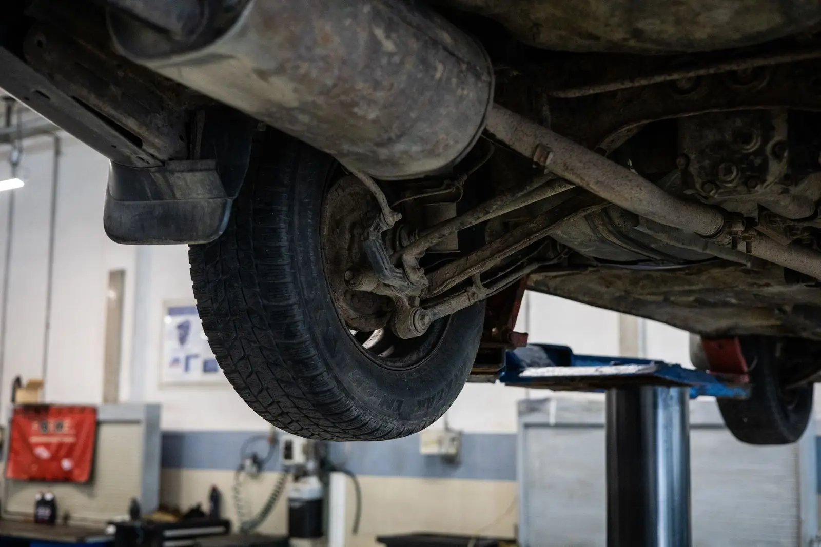 The underside of a car on a lift, showing a rear wheel, suspension arms and the exhaust running under the floor